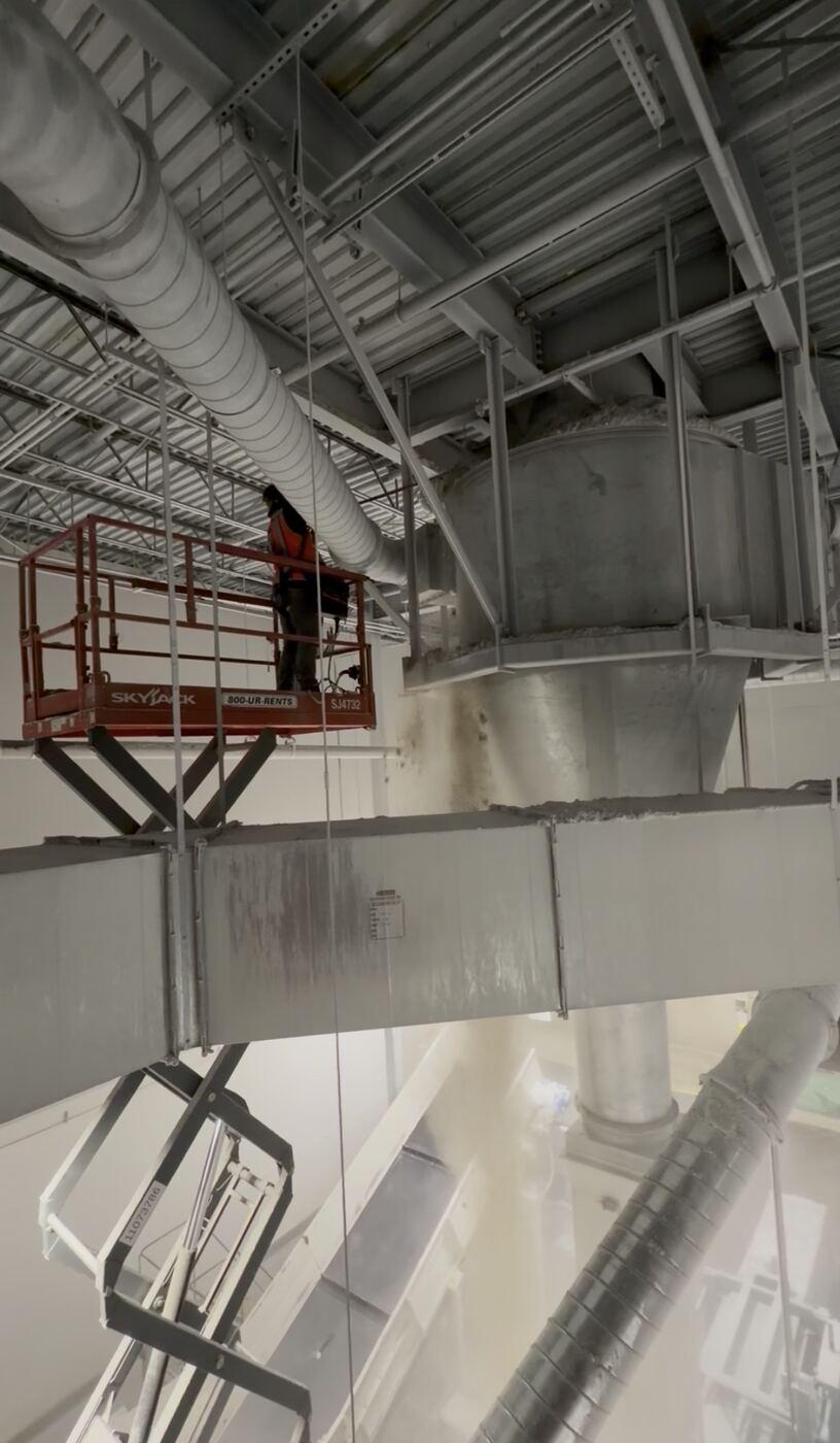 Ludlow crew member on an elevated lift cleaning combustible dust from overhead industrial structures