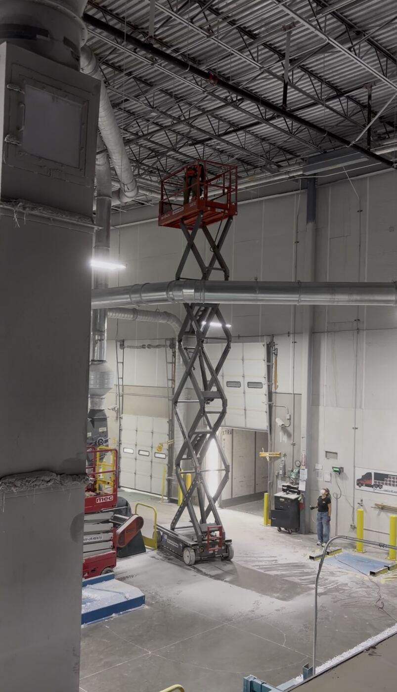 Scissor lift raised to reach overhead ductwork in a high-ceiling industrial facility